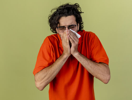 橄榄年轻的病人戴着眼镜 拿着餐巾 手放在嘴上 打喷嚏 隔离在橄榄绿的墙上 留着复印空间人疾病手
