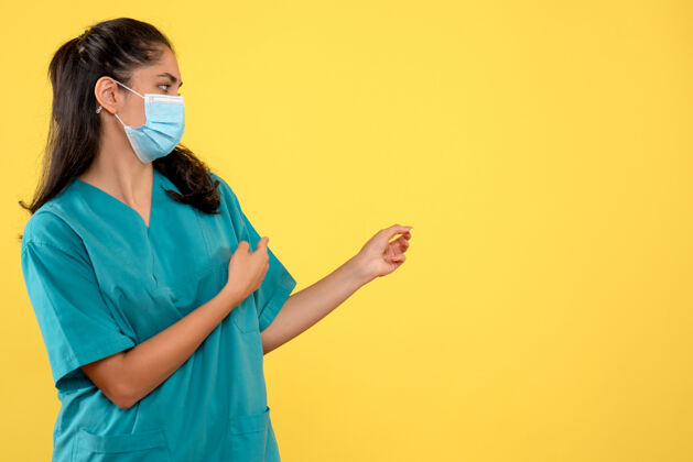 面具正面图：戴着医用面罩的女医生指着黄色的复印空间手指向女医生