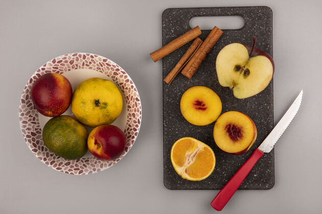 板新鲜的半个桃子放在一个黑色的厨房板上 上面有橘子和苹果 刀子放在一个灰色背景的碗上 上面有桃子和橘子食物一半顶部