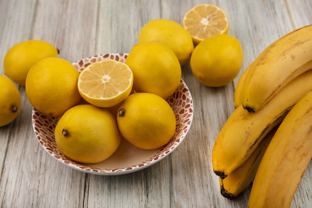 观点顶视图黄色皮肤的整个柠檬上的一个碗香蕉隔离在灰色的木制背景健康整个水果