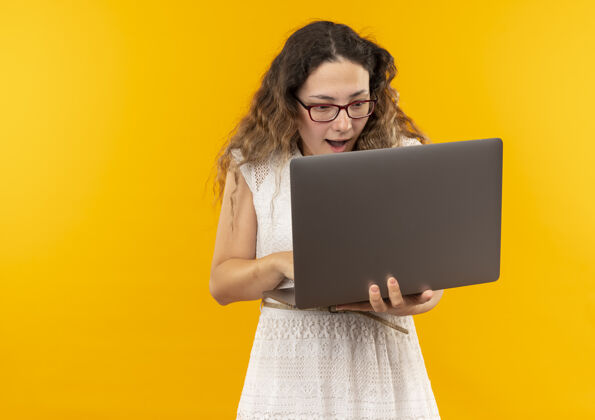 使用印象深刻的年轻漂亮的女学生戴眼镜和背包使用笔记本电脑隔离在黄色印象眼镜笔记本电脑