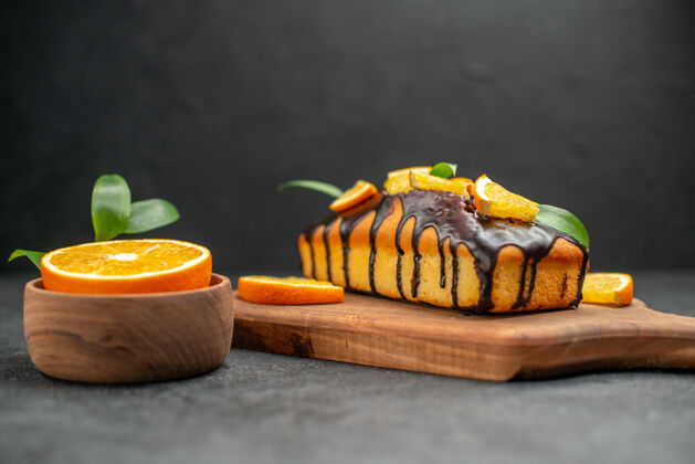 切切菜板上的软蛋糕和深色桌子上的带叶子的切橘子的侧视图盘子食物面包