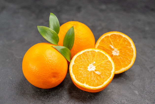套装在黑暗的桌子上的一套黄色的完整的和切碎的橙子的特写镜头深色封闭可食用水果