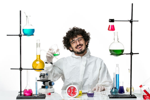 化学品前视图穿着特殊套装的年轻男性科学家坐在白墙上 用不同的解决方案套装实验室容器