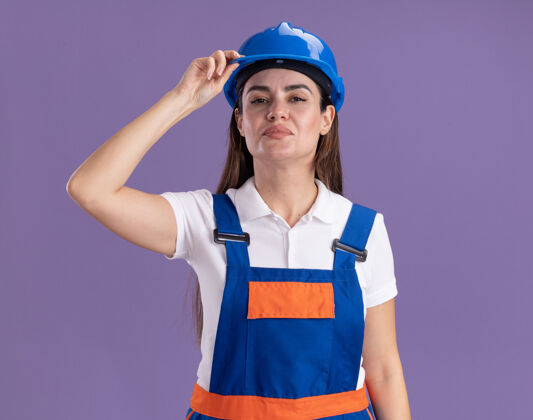 建设者自信的年轻建设者 身着制服 戴着安全帽 孤零零地站在紫色的墙上头盔年轻制服