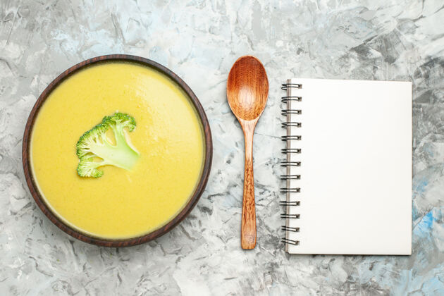 餐具俯瞰图奶油西兰花汤在一个棕色的碗和勺子旁边的笔记本在灰色的桌子上勺子厨房西兰花汤