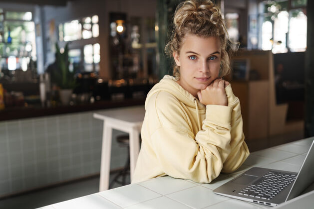 金发一个年轻漂亮的女人独自坐在咖啡馆里 手里拿着一台笔记本电脑工作聊天学生