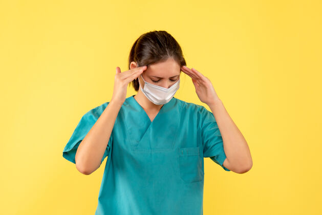 视图正面图黄色背景上穿着医用衬衫 戴着无菌口罩 头痛的女医生病毒绝育面具