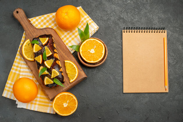健康俯视整个软蛋糕和切柠檬叶子旁边的笔记本在黑暗的桌子上柑橘叶子可食用水果