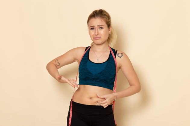 锻炼正面图：穿着运动服的年轻女性测量她的身体由于体重而悲伤美丽测量风景