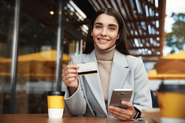 转移坐在咖啡店里用信用卡和手机在线支付的年轻女子咖啡馆钱单独