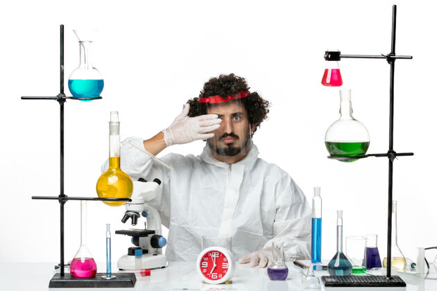穿着正面图年轻的男科学家穿着特殊的西装 戴着防护头盔 在白色的办公桌上工作 科学实验室里充满了男性化学特殊实验室套装