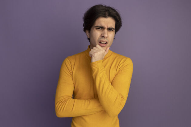 高领毛衣困惑的年轻帅哥穿着黄色高领毛衣把手放在下巴下孤立在紫色的墙上困惑毛衣男人