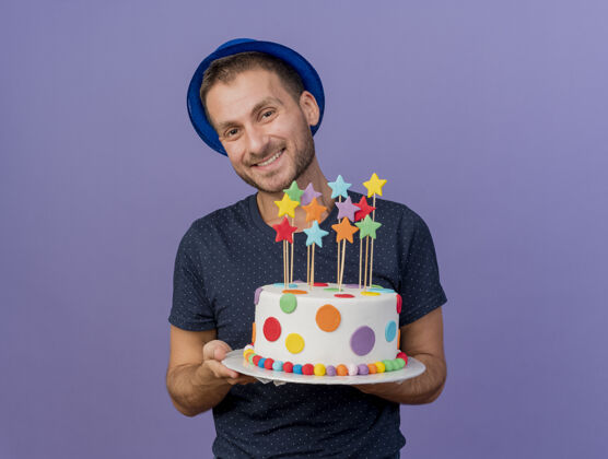 复制微笑英俊的白人男子戴蓝色帽子举行生日蛋糕上紫色的背景与复制空间隔离蛋糕微笑空间