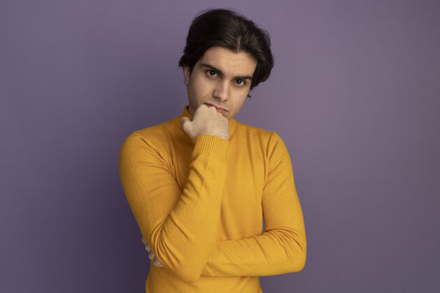 毛衣自信的年轻帅哥穿着黄色高领毛衣把拳头放在下巴上隔离在紫色的墙上穿拳头自信