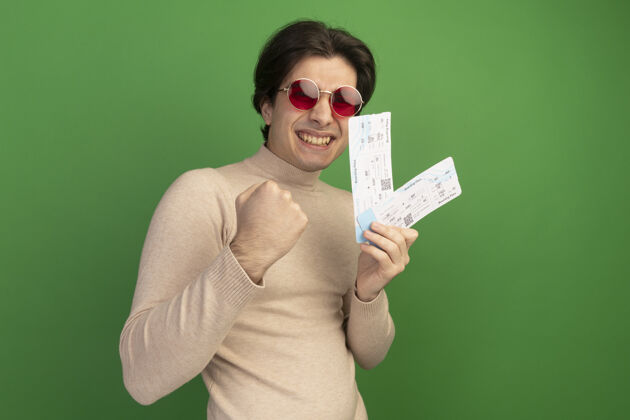 眼镜戴着眼镜的年轻帅哥微笑着 手里拿着绿墙上显示“是”手势的票票年轻人手势