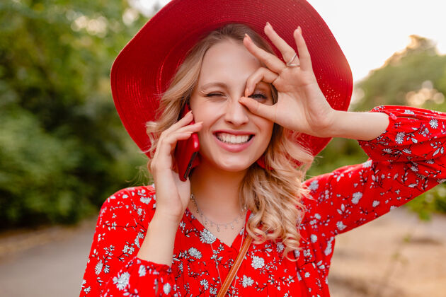 金发迷人的时尚金发微笑的妇女在稻草红色帽子和衬衫夏季时尚服装画像在电话交谈积极的姿态情感装束脸明亮