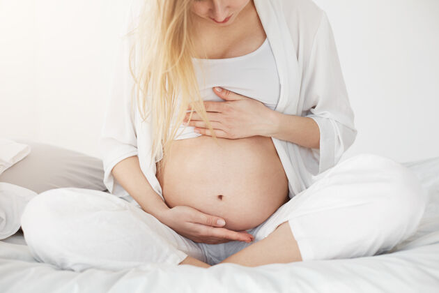 年轻人金发碧眼的孕妇看着自己的肚子 用手支撑着肚子 等待她的男婴或女婴的到来坐着女人房子