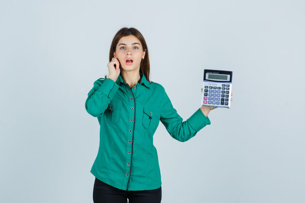 压抑年轻的女士拿着计算器 一边拉下她的耳垂 穿着绿色衬衫 神情焦急 前视衬衫成人肖像