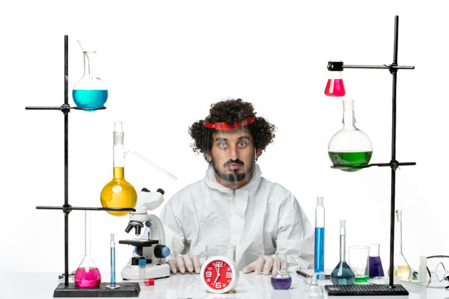 套装正面图身穿特殊套装的年轻男科学家戴着特殊的防护头盔站在白色的墙上瓶子实验室化学