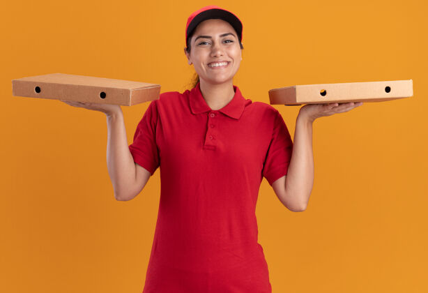 送货微笑的年轻送货女孩穿着制服 戴着帽子 拿着披萨盒孤立在橙色的墙上披萨年轻人女孩