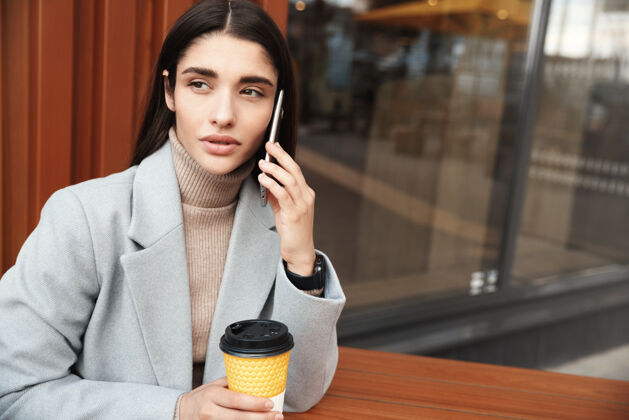 街道坐在咖啡馆里用手机聊天的女人在咖啡馆工作的女商人和客户聊天城市外套手机