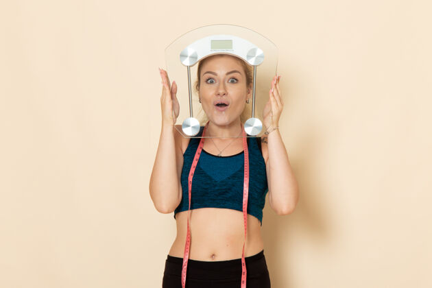 年轻女性正面图身着运动装的年轻女性手持天平在白色墙壁上健身运动美容保健操服装尺度身体