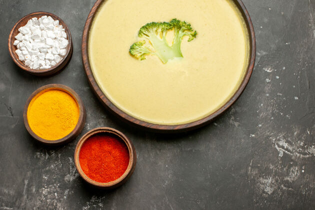 碗俯瞰图奶油西兰花汤在一个棕色的碗和不同的香料在灰色的桌子上头顶盘子汤碗