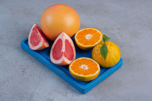 美味把整个橘子和葡萄柚片放在一个蓝色的小托盘上 放在大理石背景上美味配料托盘