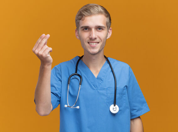听诊器微笑的年轻男医生穿着医生制服 听诊器显示提示手势孤立在橙色墙上男性制服提示