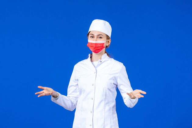 人正面图身着医疗服的年轻护士 蓝色墙上戴着红色防护面具医红病毒