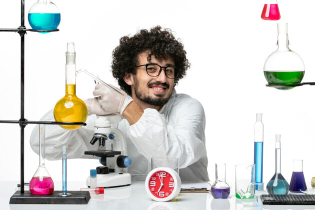 男人正面图身着特殊套装的年轻男科学家拥抱显微镜 微笑着站在白墙上医学显微镜套装