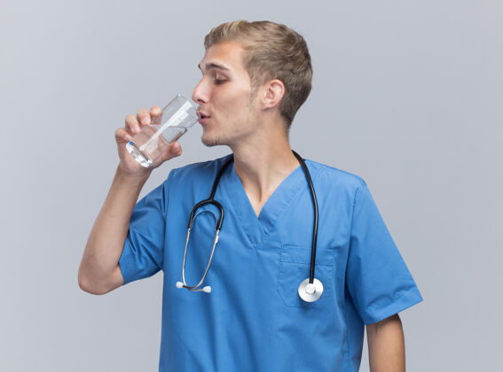 请穿高兴的年轻男医生穿着医生制服用听诊器喝水隔离在白墙上水医生年轻