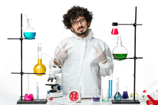 实验室正面图身穿白色特殊套装的年轻男性科学家站在桌子旁 拿着解决方案大流行科学套装