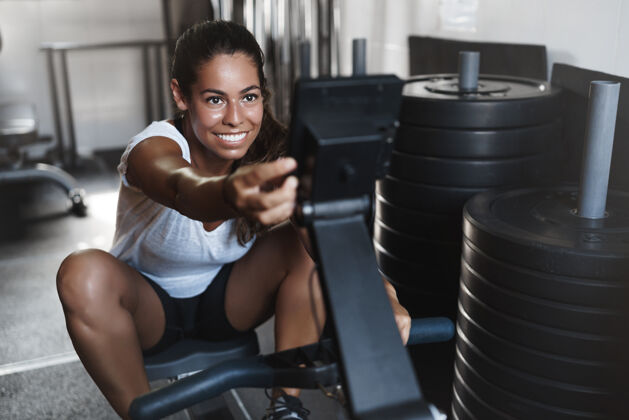 年轻积极的年轻女运动员 在健身房微笑 使用压腿设备人决心能量