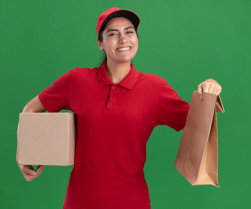 纸张微笑的年轻送货女孩穿着制服 戴着帽子 拿着一个纸食品包装盒 隔离在绿色的墙上女孩年轻人穿着