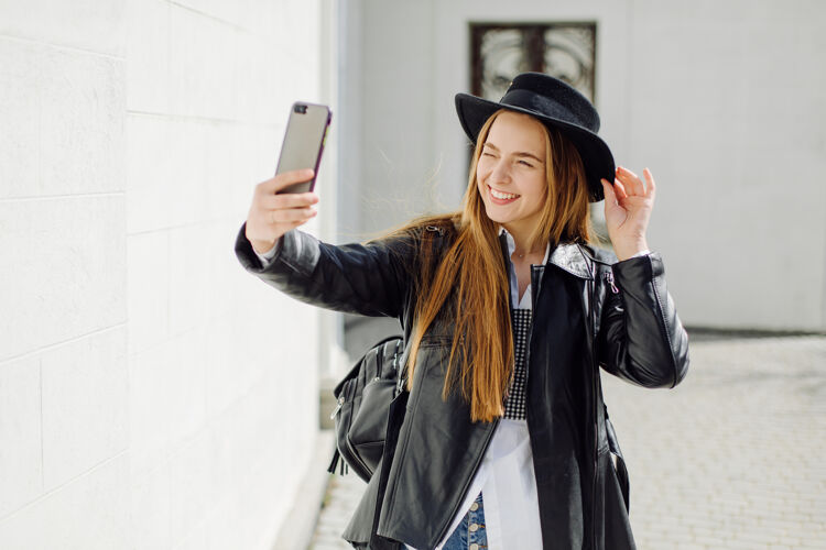 女人户外夏日写真的年轻时尚女孩在阳光明媚的日子摆在街上与手机移动触摸墙
