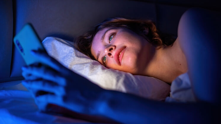 放松小女孩在床上用智能手机房间里有蓝色的照明女人女人床