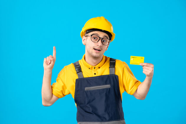 制服身穿黄色制服 信用卡在蓝色上的男工人的正面视图工作建筑修理工