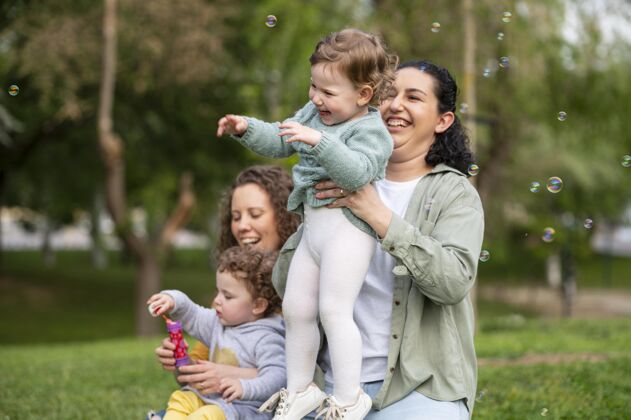 肥皂泡微笑宝宝在户外公园与同性恋母亲女人在一起夫妇