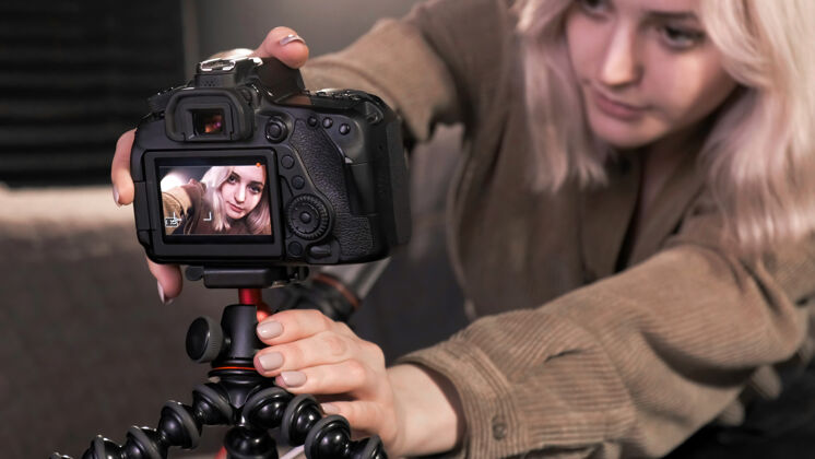 按钮年轻的内容创作者金发女孩把相机放在三脚架上 拍摄自己为vlog说话技术媒体自由职业者