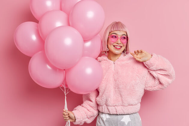 气球快乐好看的亚洲女模特 粉色头发 穿着冬季皮草外套 戴着时髦的心形太阳镜 手持气球 准备庆祝特殊场合节日活动概念女士女性梦幻