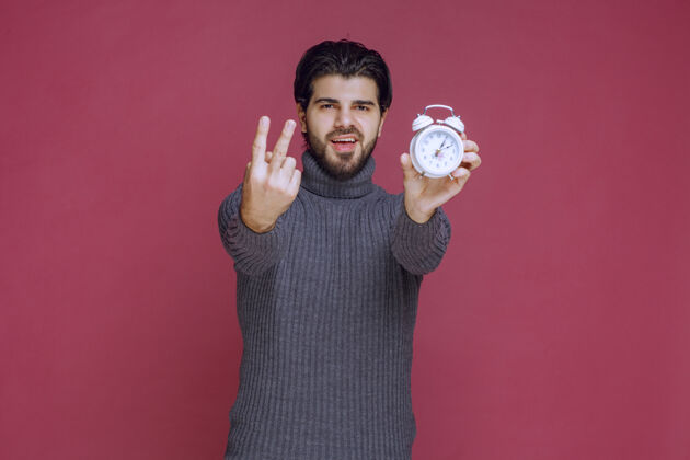 照片一个男人拿着一个白色闹钟 指着一个最好的报价年轻男性人体模型