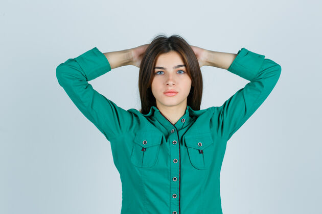 成功年轻的女性手牵手在头后 穿着绿色衬衫 看起来很自豪 正面视图手姿势商业