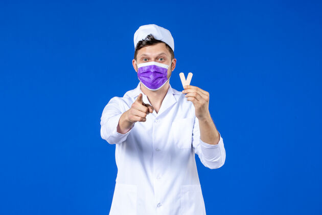 疫苗前视图中的男医生穿着医疗服 戴着面罩 手里拿着小药片 指着蓝色的你指点医院药品