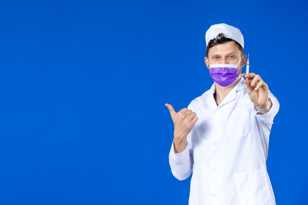 药品身穿医疗服 戴着紫色口罩的男医生正对着蓝色的脸拿着针剂大流行药品病毒