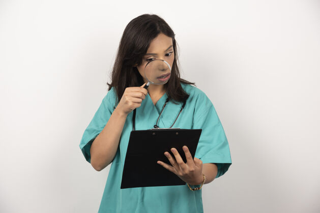 工人女医生用放大镜在白色背景上紧张地看着剪贴板工作剪贴板听诊器