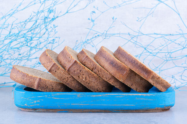 面包把棕色面包片放在大理石表面的蓝色盘子里酵母烘焙食品营养