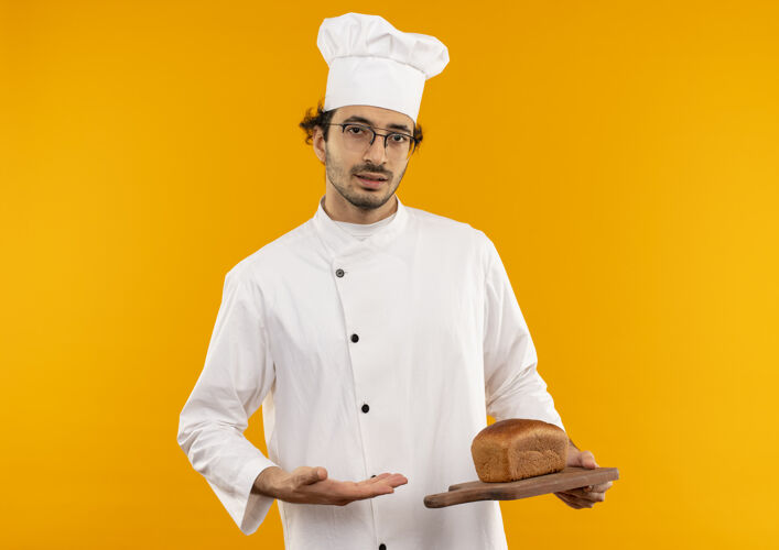 眼镜年轻的男厨师身穿厨师制服 手持眼镜 用手指着切板上的面包制服切厨师