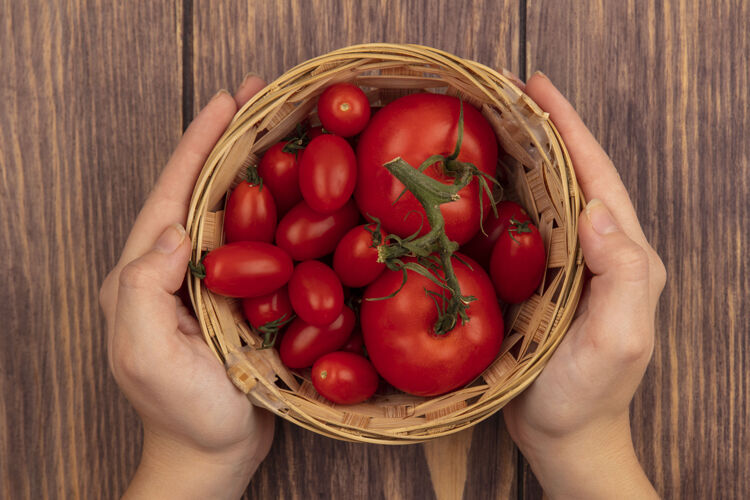新鲜顶视图女性手拿着一桶新鲜的西红柿在木制表面有机饮食营养
